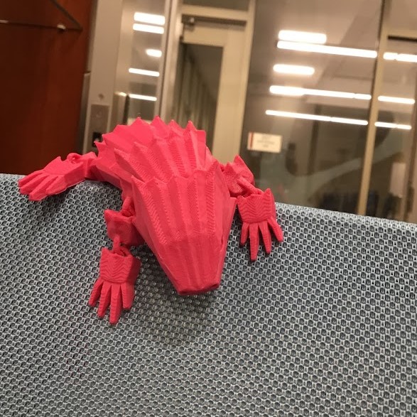 pink 3d printed bendy lizard on the back of a grey chair